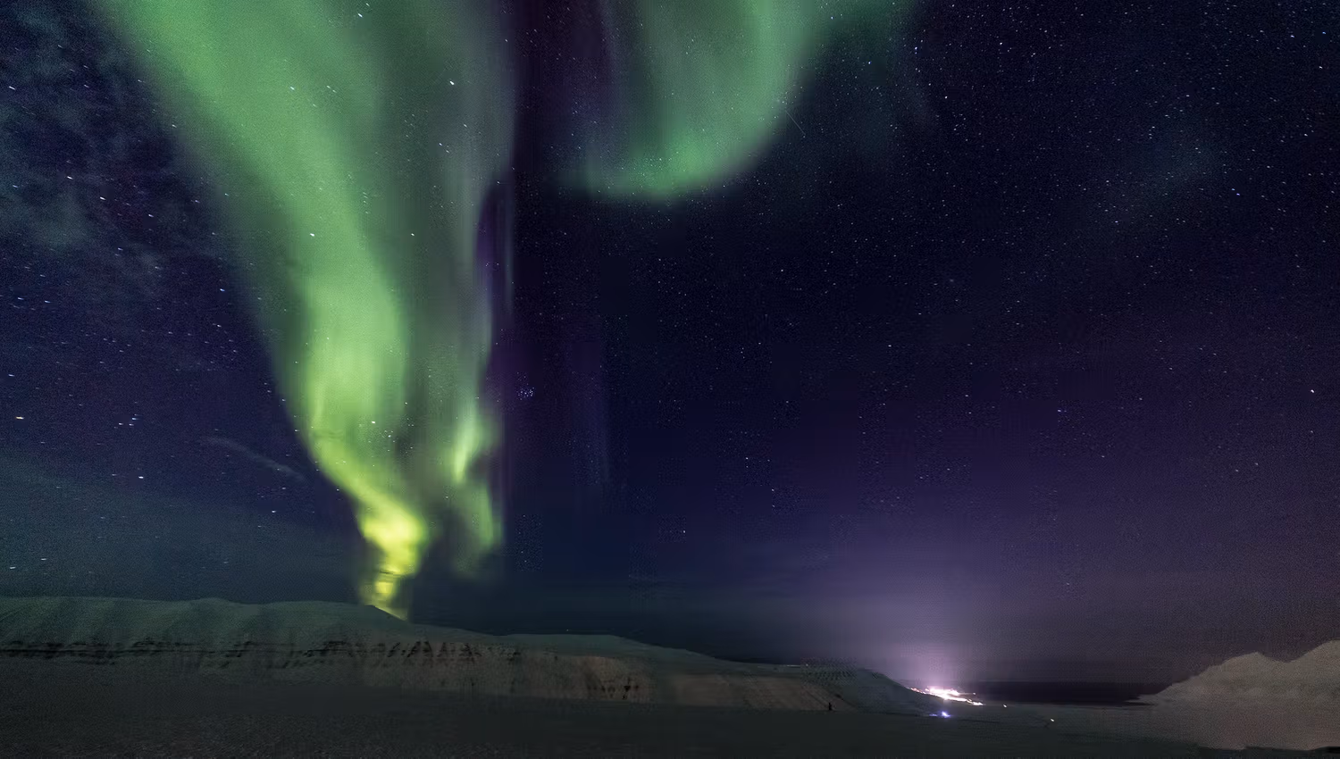 A stripe of green northern lights dancing above the snowcovered mountains