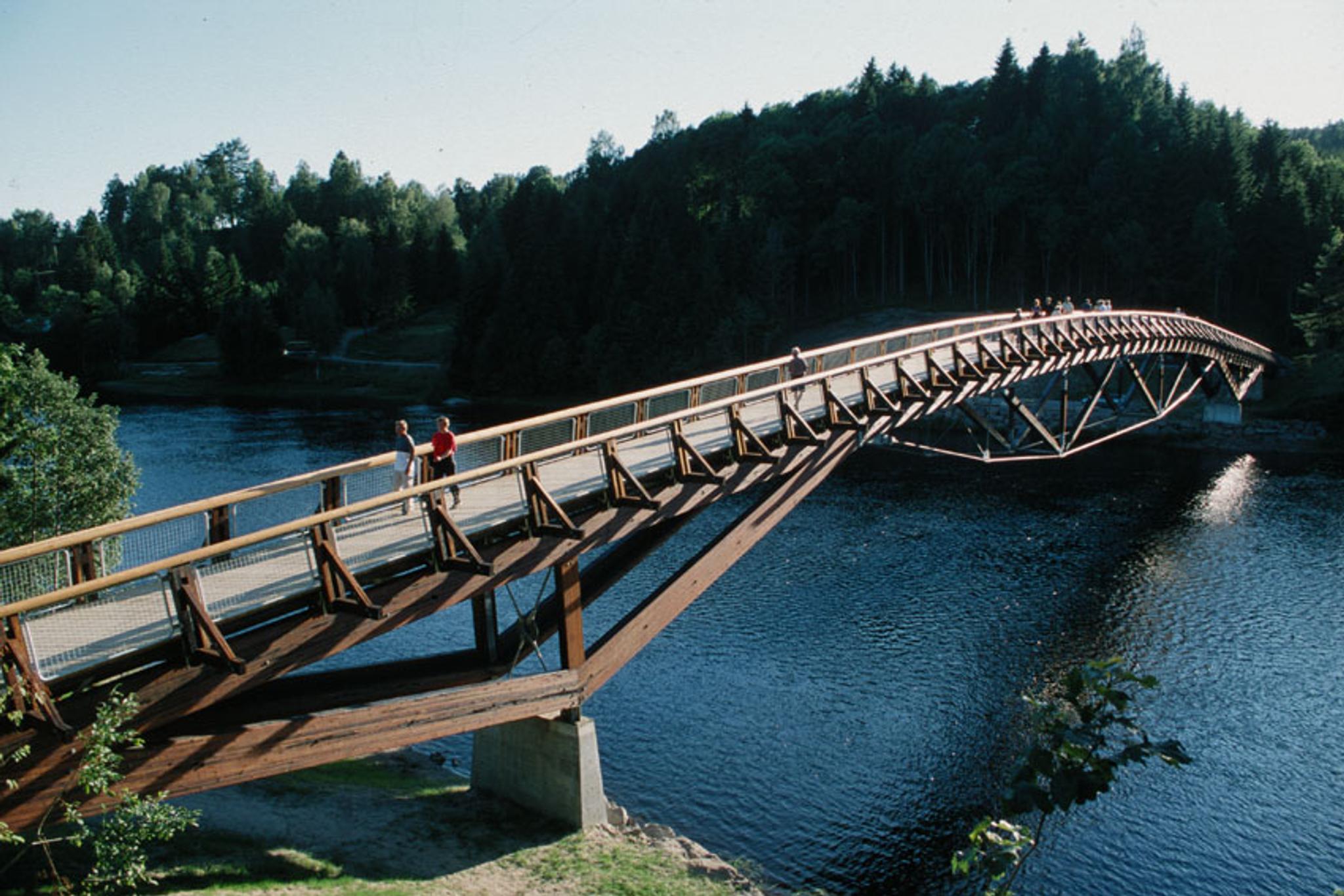 Several people cross a bridge with Numedalslågen flowing underneath.