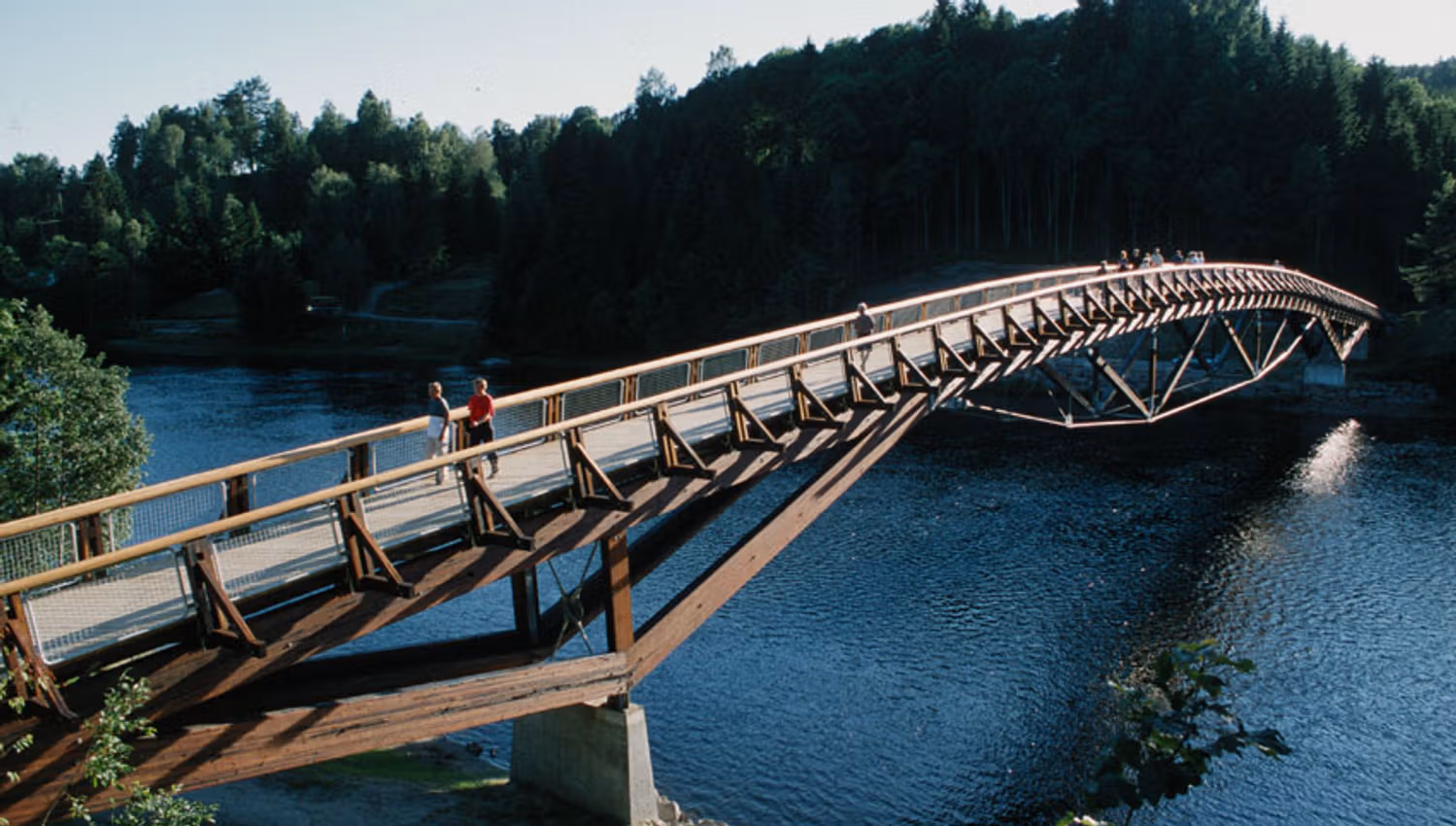 Several people cross a bridge with Numedalslågen flowing underneath.