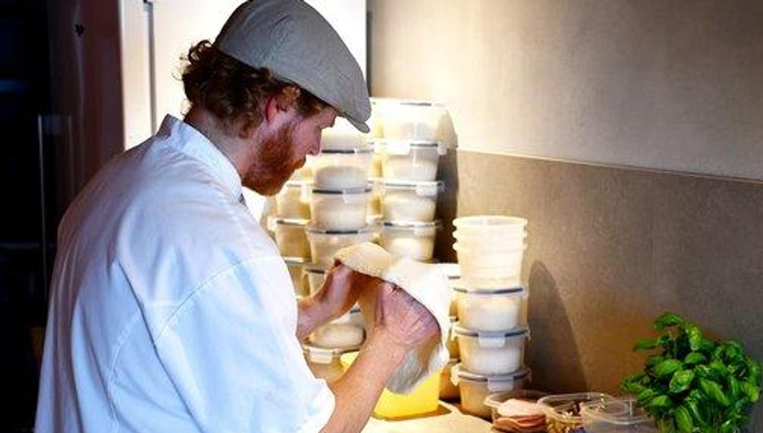A man seen from the side, stretching out a pizza dough.