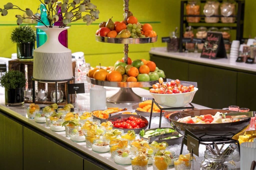 Buffet table with fruit, vegetables, and small dessert glasses with yoghurt and fruit.