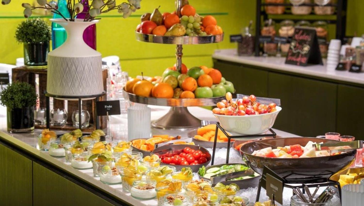 Buffet table with fruit, vegetables, and small dessert glasses with yoghurt and fruit.