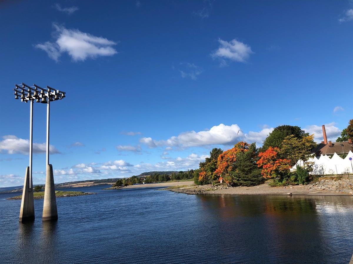 Skibladnerbrygga in Hamar city center. A clear view of Lake Mjøsa featuring the distinctive bell sculpture rising from the water, framed by blue sky a