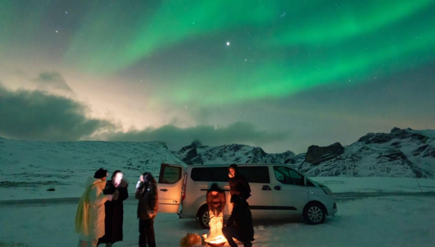 Guests in fron a minibus taking pictres of the northern lights above.