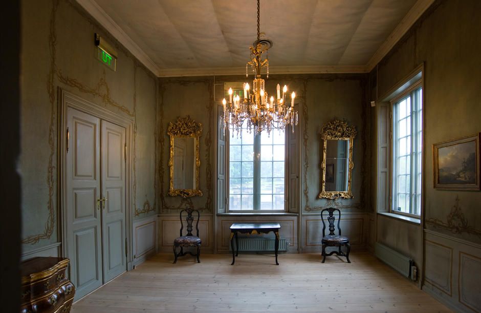 Old interior with a chandelier hanging from the ceiling, mirrors and paintings on the walls.
