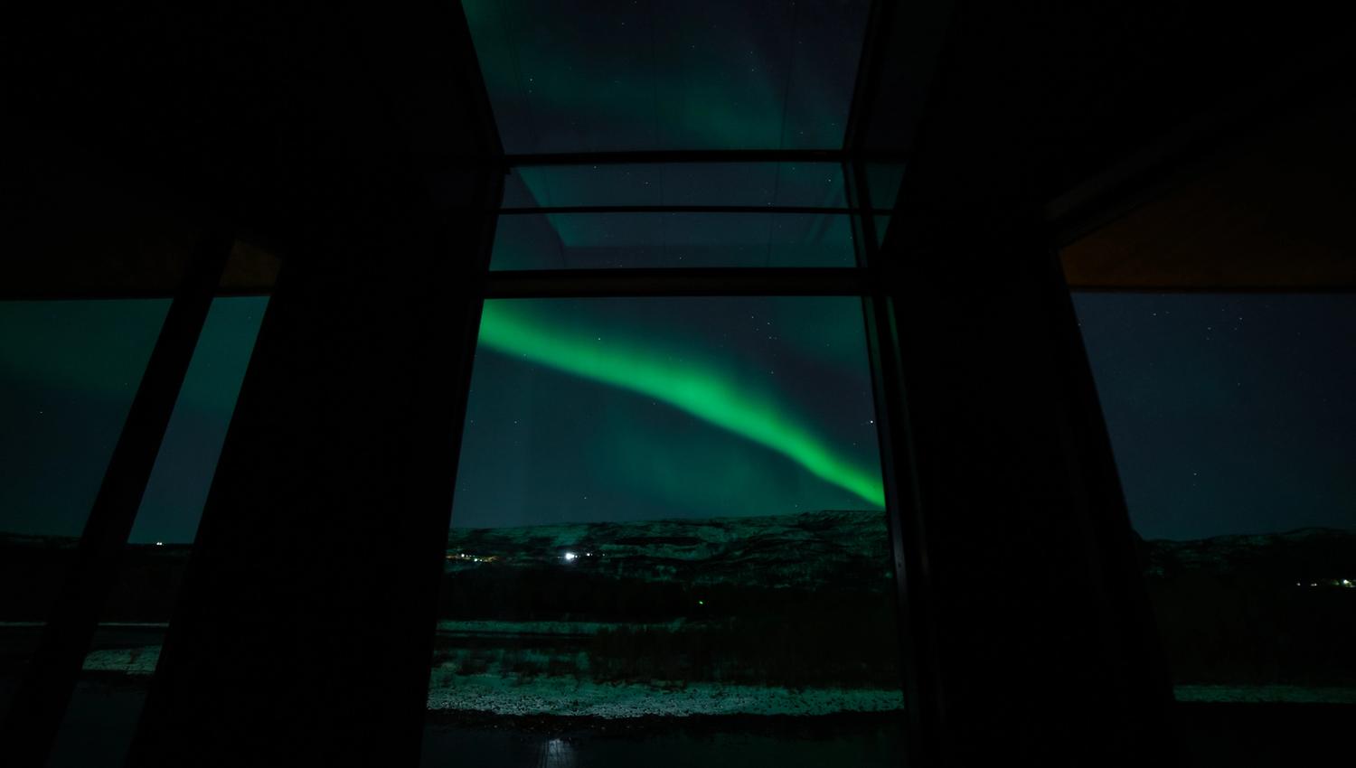 Aurora borealis visible through large windows, snow-covered landscape below.