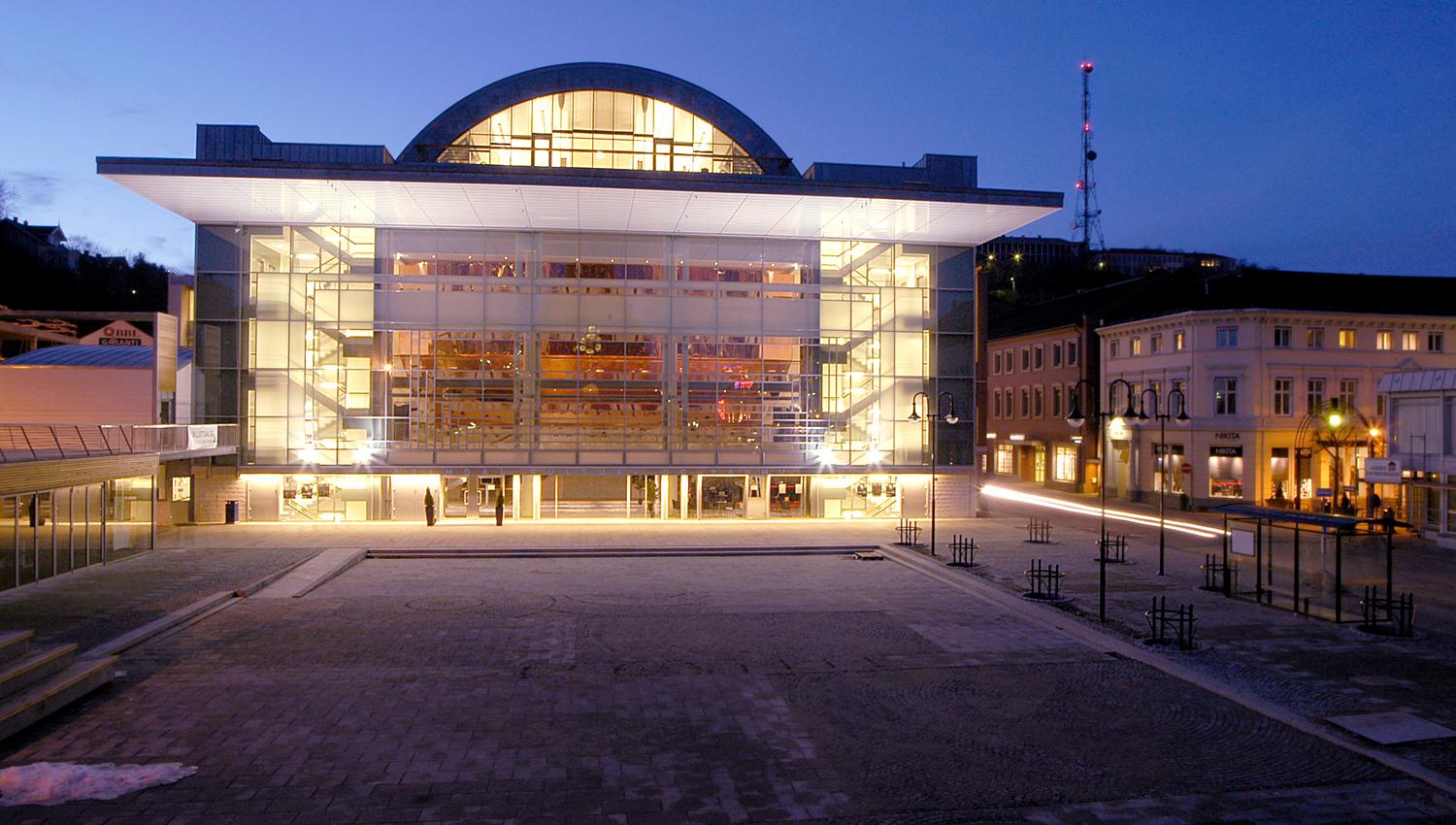 Arendal Kultur- og rådhus med opplyst frontfasade i skumringen.