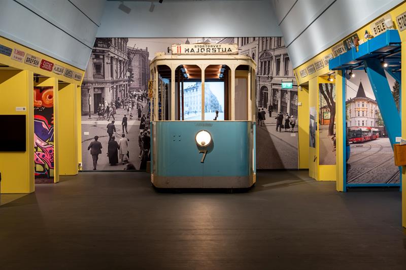 Museum exhibition featuring a restored tram set against historic photographs of Oslo streets and displays about the history of public transport.