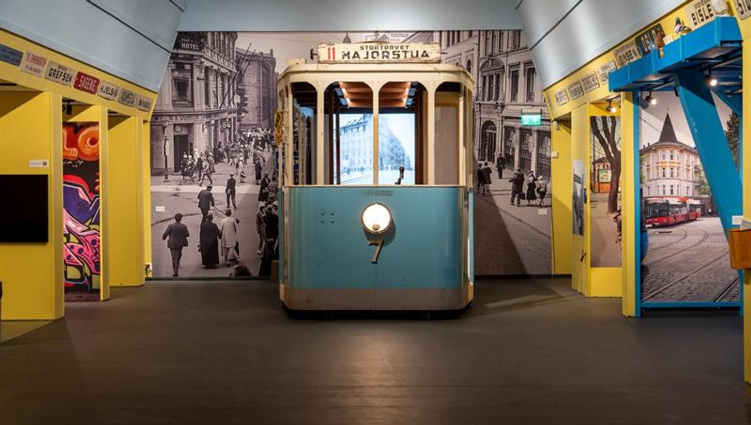 Museum exhibition featuring a restored tram set against historic photographs of Oslo streets and displays about the history of public transport.