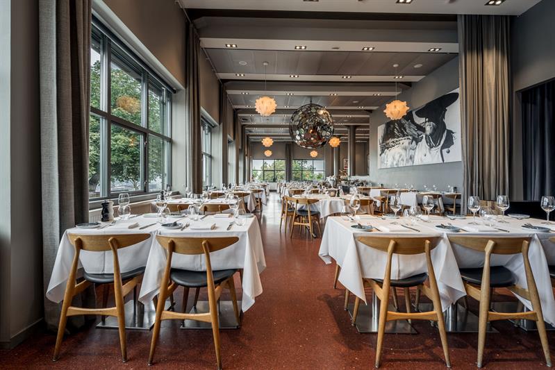 Romslig restaurant med oppdekkede bord, designlamper og utsikt gjennom store vinduer.