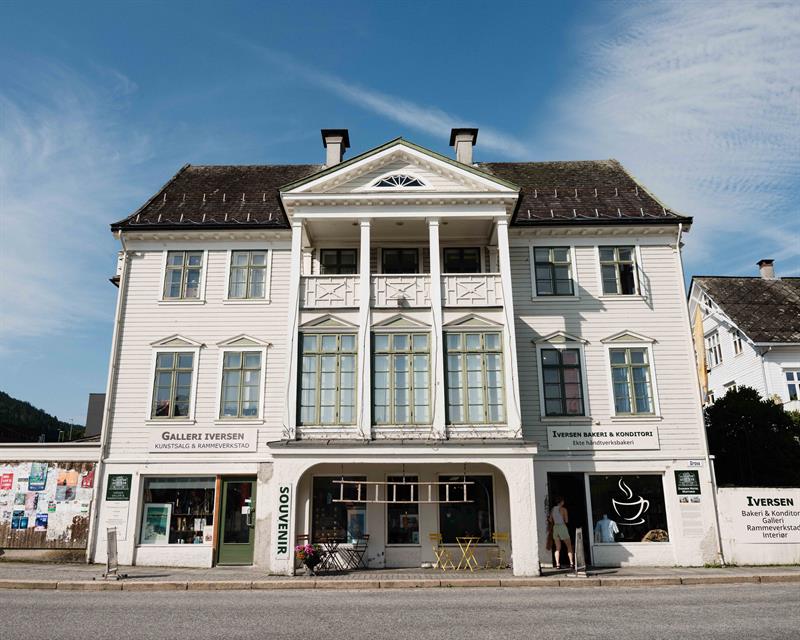 The façade of Iversen Bakery and Gallery in Norheimsund shows the white wooden building with bakery, gallery and outdoor seating along the street.
