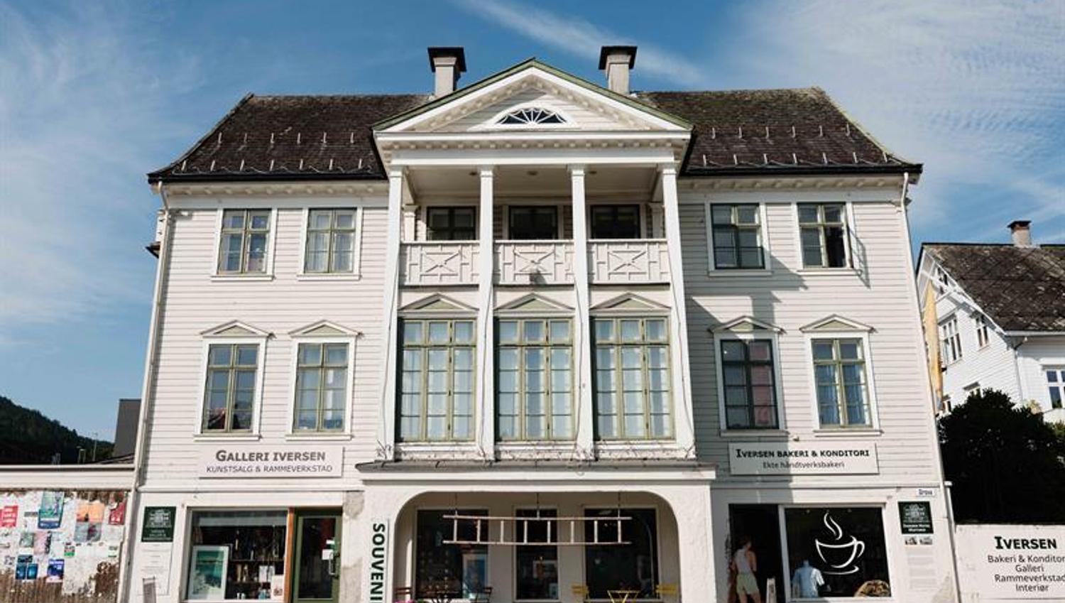 The façade of Iversen Bakery and Gallery in Norheimsund shows the white wooden building with bakery, gallery and outdoor seating along the street.