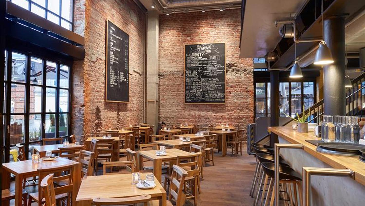 Restaurant interior with a high ceiling, a bar counter, dinner tables and chairs.