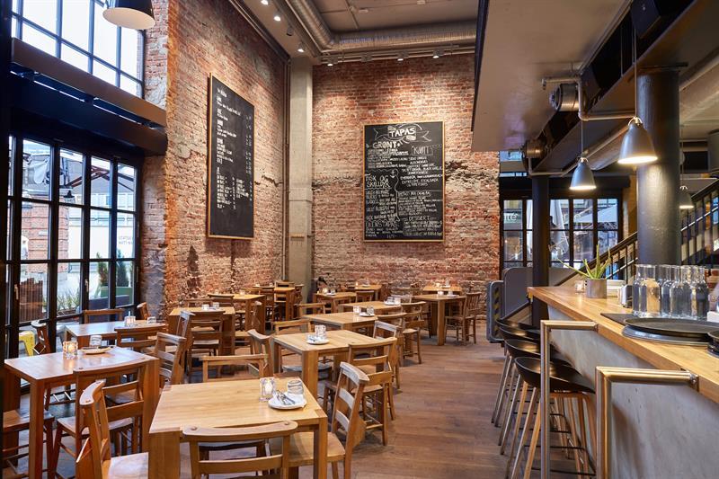 Restaurant interior with a high ceiling, a bar counter, dinner tables and chairs.