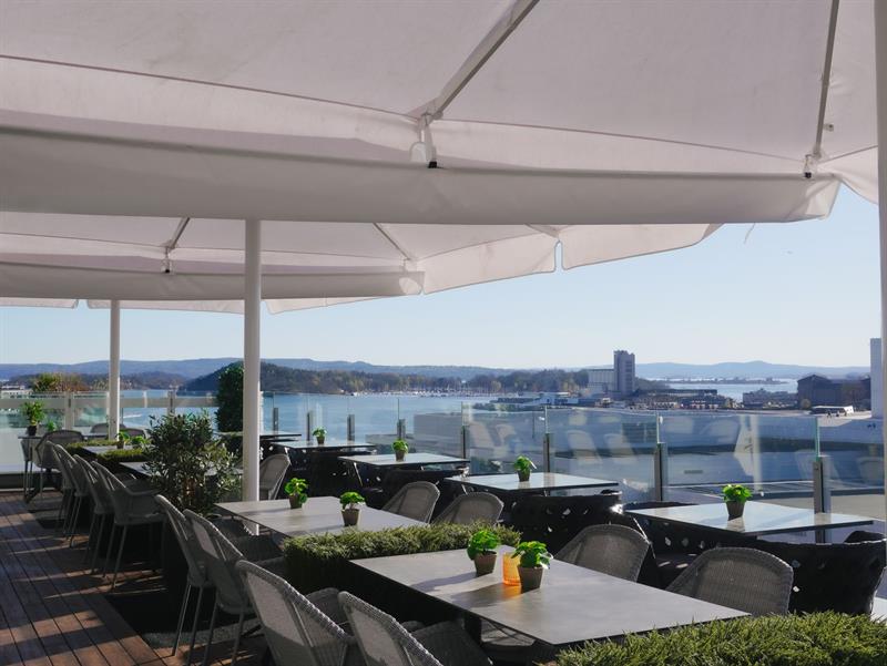 Stylish rooftop terrace with tables, glass railings and views towards the fjord.