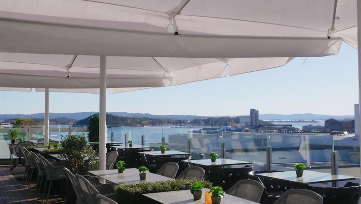 Stylish rooftop terrace with tables, glass railings and views towards the fjord.