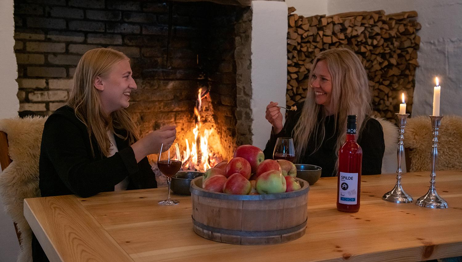 Two guests enjoying apple cider and dessert by the fireplace at Eldhuset Farm Restaurant in Hardanger.