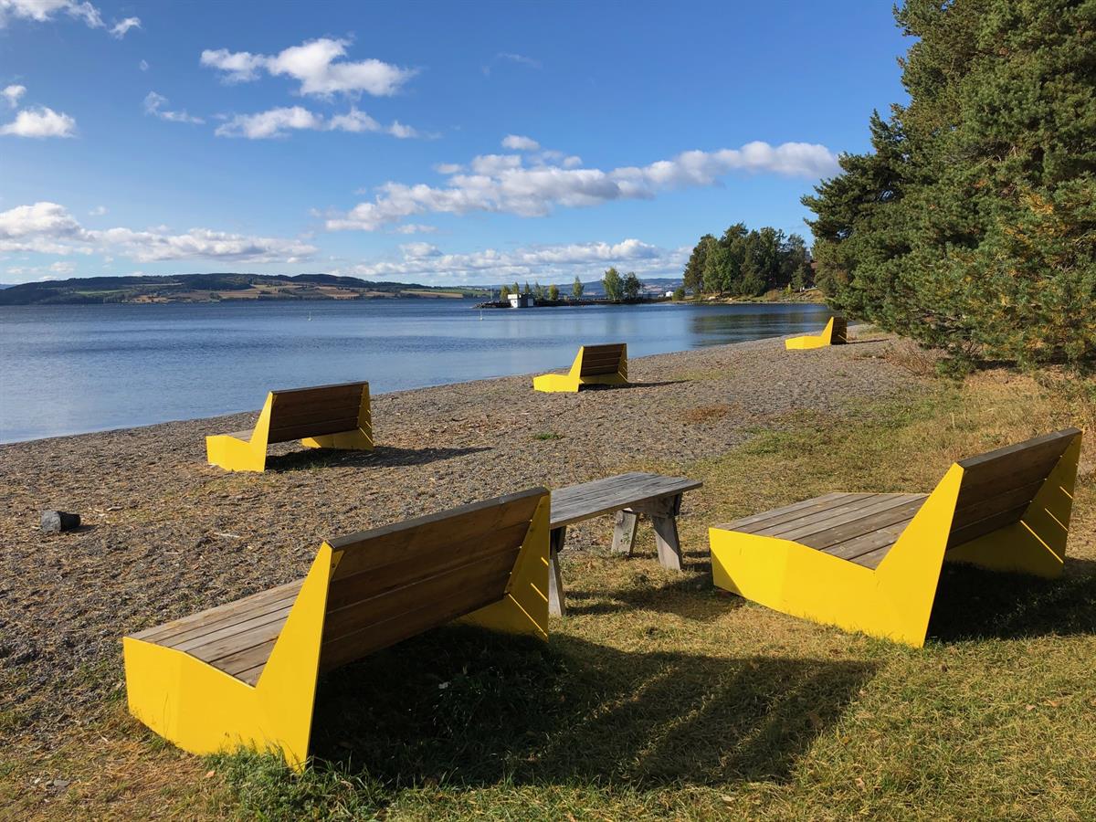 En strand med gule benker og bord plassert ved vannet på en solrik dag.