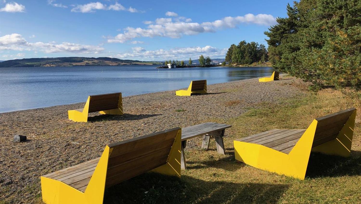 En strand med gule benker og bord plassert ved vannet på en solrik dag.