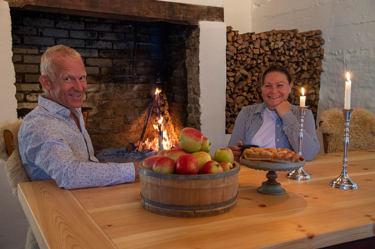 Hosts at Eldhuset Farm Restaurant welcoming guests with homemade apple cake and cider.