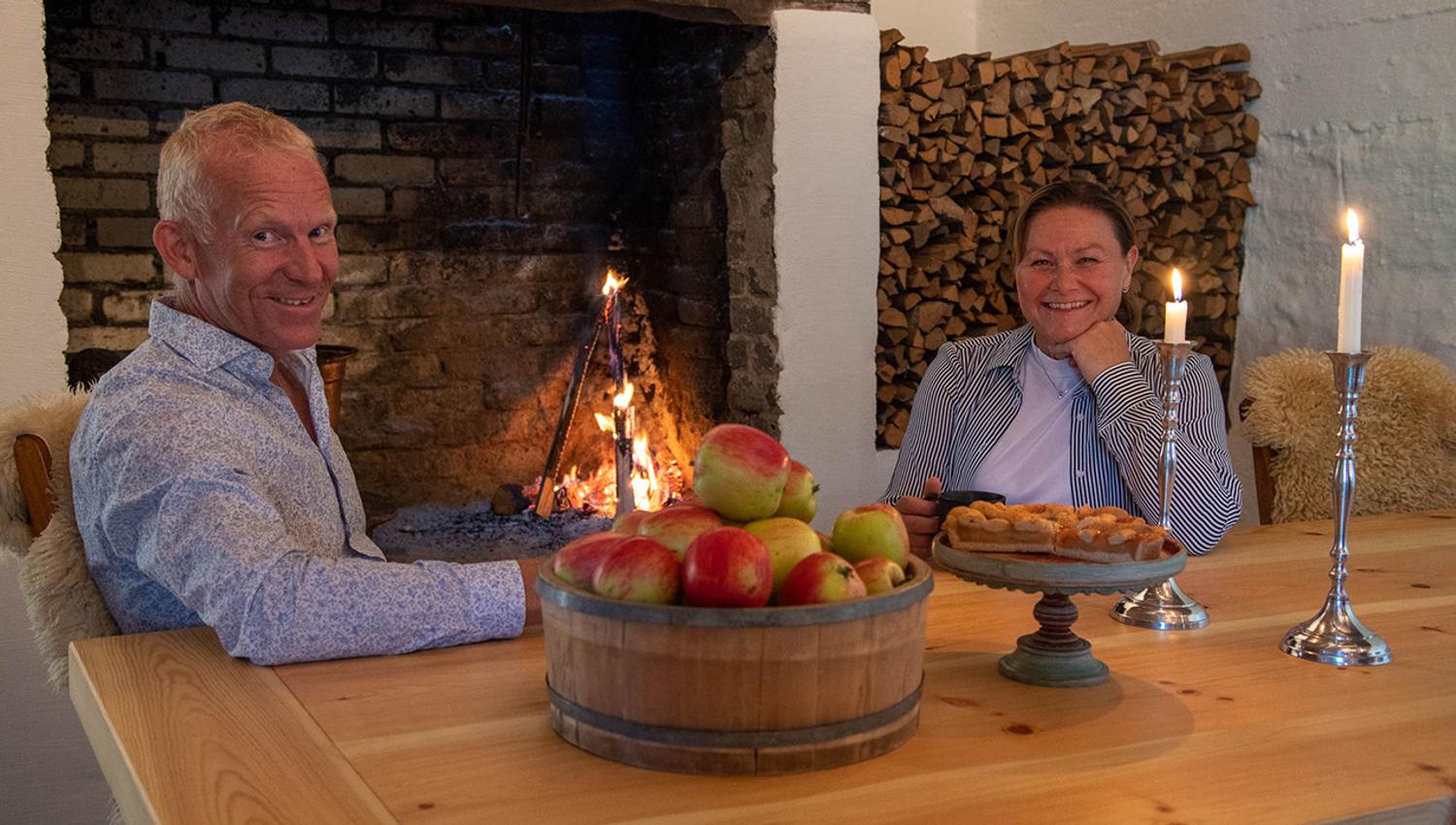 Hosts at Eldhuset Farm Restaurant welcoming guests with homemade apple cake and cider.