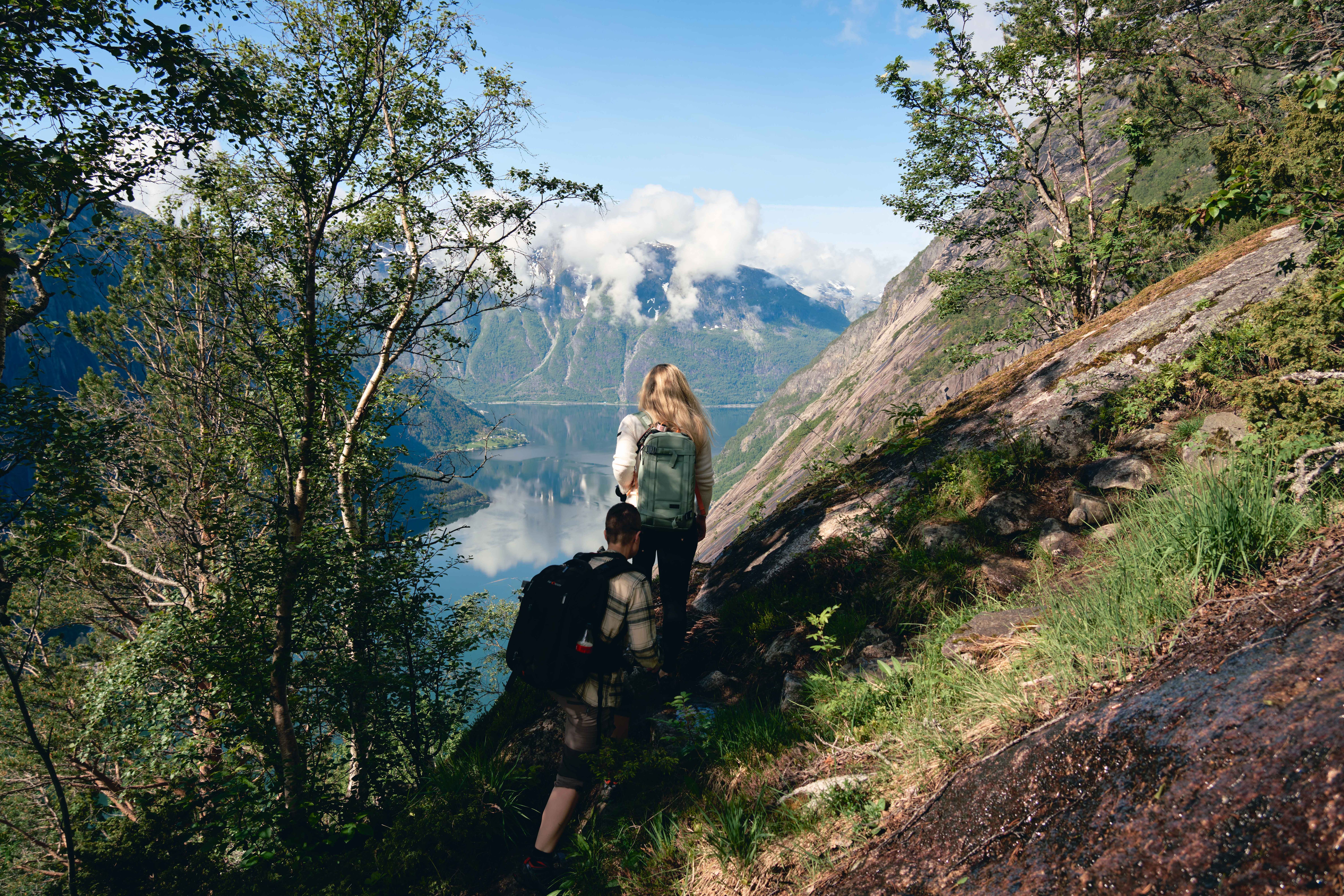 Two women hiking the steep Kjeåsen path, with the fjord and mountains in the background.