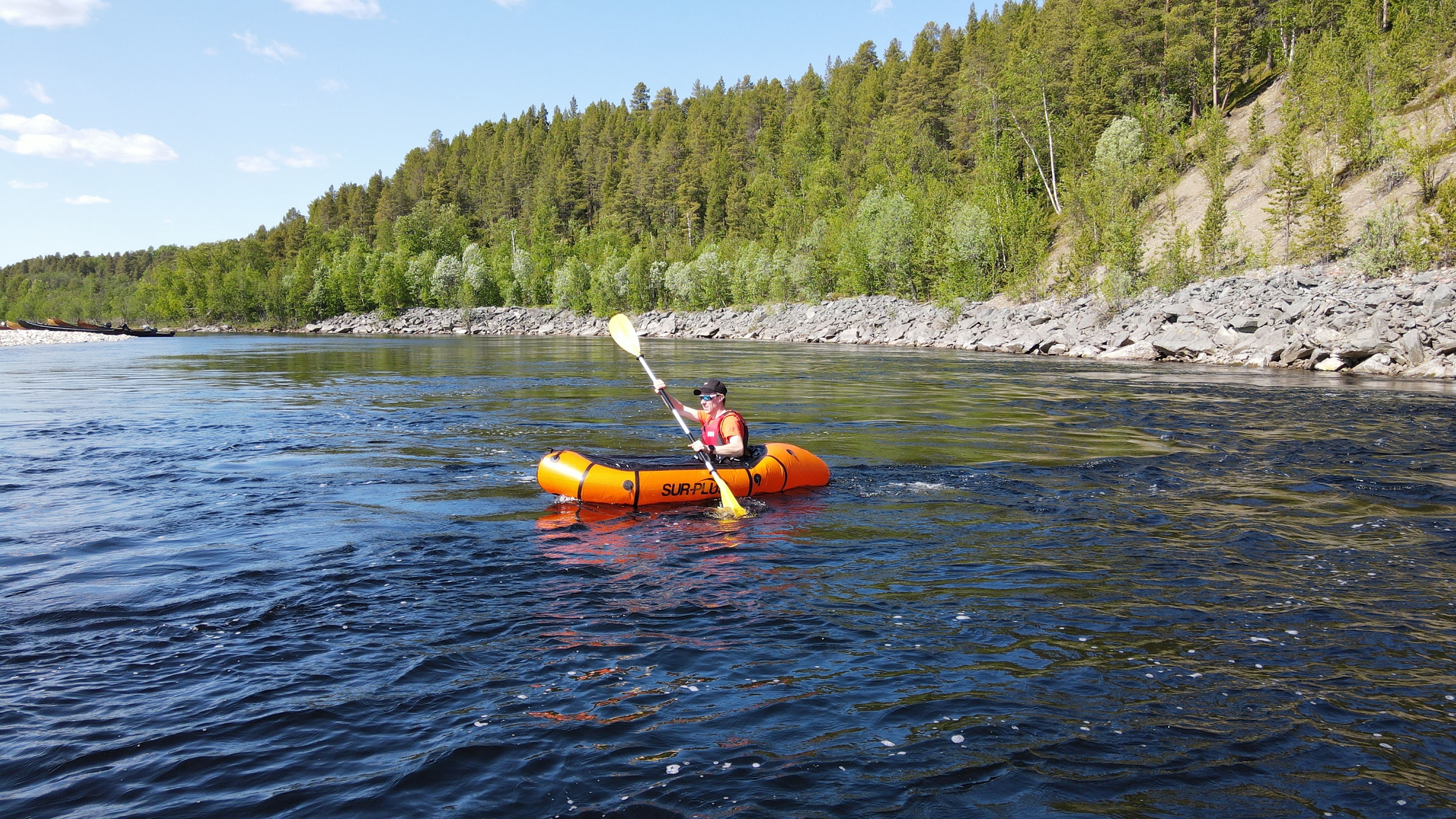 Un kayakiste pagayant sur une rivière entourée d'arbres verdoyants.