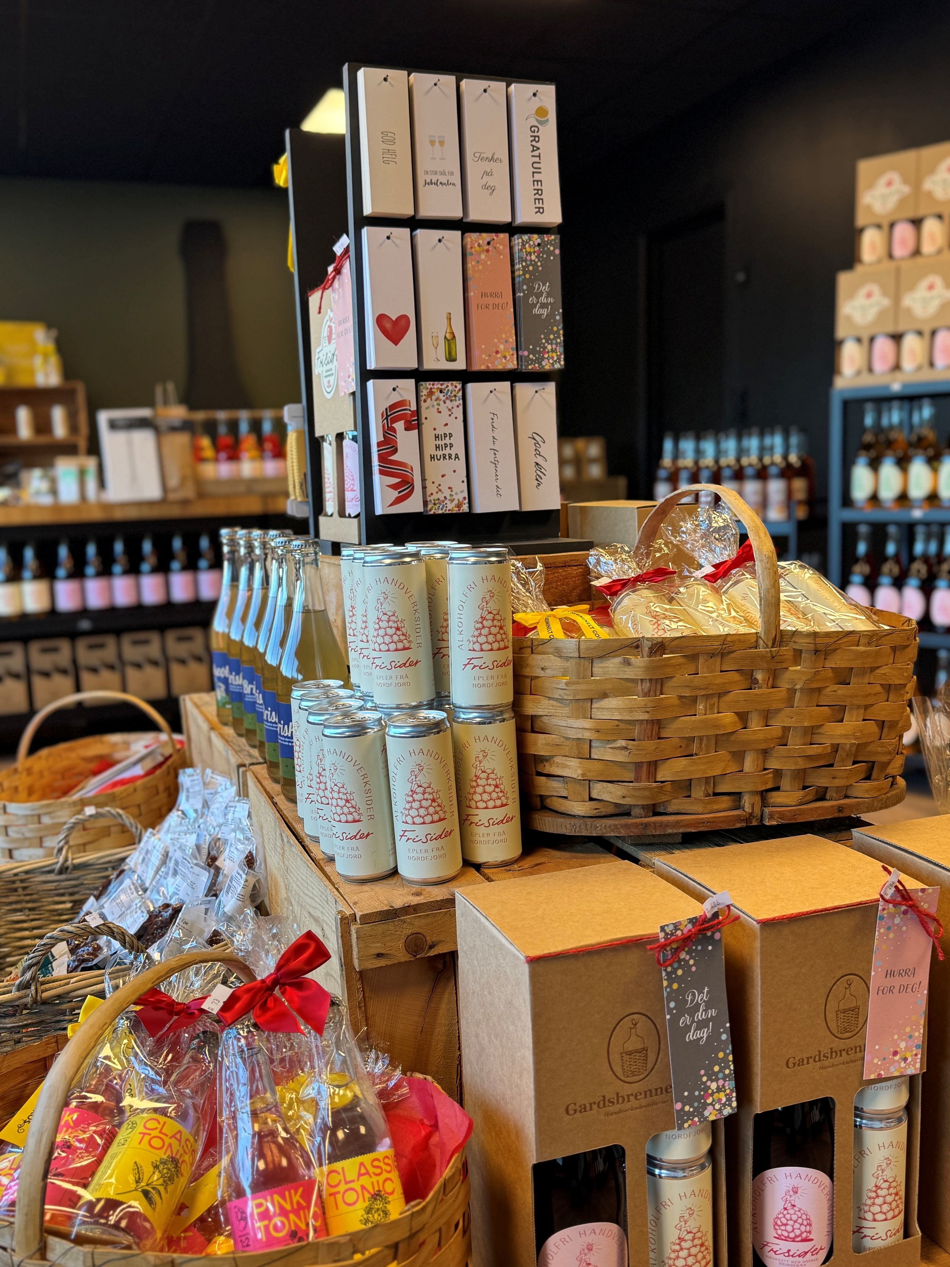 Store counter display with gift baskets, boxed sets, bottles, and cider cans arranged on wooden crates.