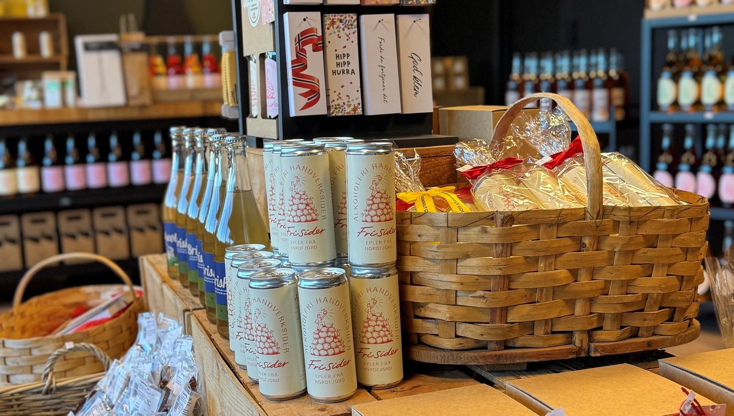 Store counter display with gift baskets, boxed sets, bottles, and cider cans arranged on wooden crates.