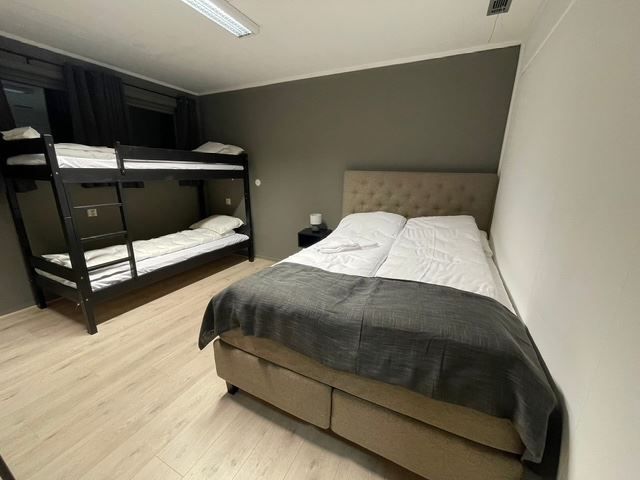 Compact bedroom with a double bed and dark throw, plus a black bunk bed, gray walls, and wood floor.