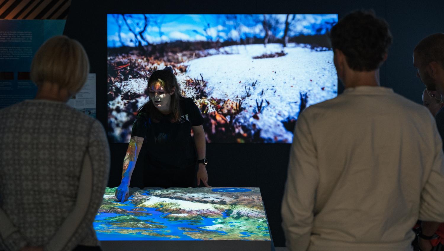 Guide pointing out key landscape features on the digital map in the “This is where we live” exhibition at Hardanger Aquaculture Centre.