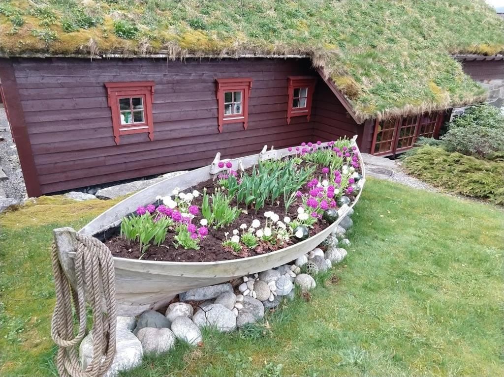 Orheimstunet in Nordfjord - A wooden boat used as a flower bed sits on rocks in a grassy yard beside a red cottage with a turf roof..