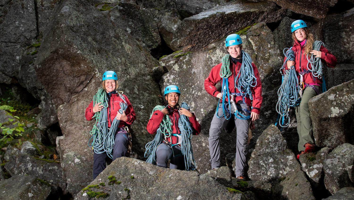 4 ansatte på Aktiv Fritid Tjøme med masse tau på skuldrene smiler mot fotografen der de står under et overhengende fjell