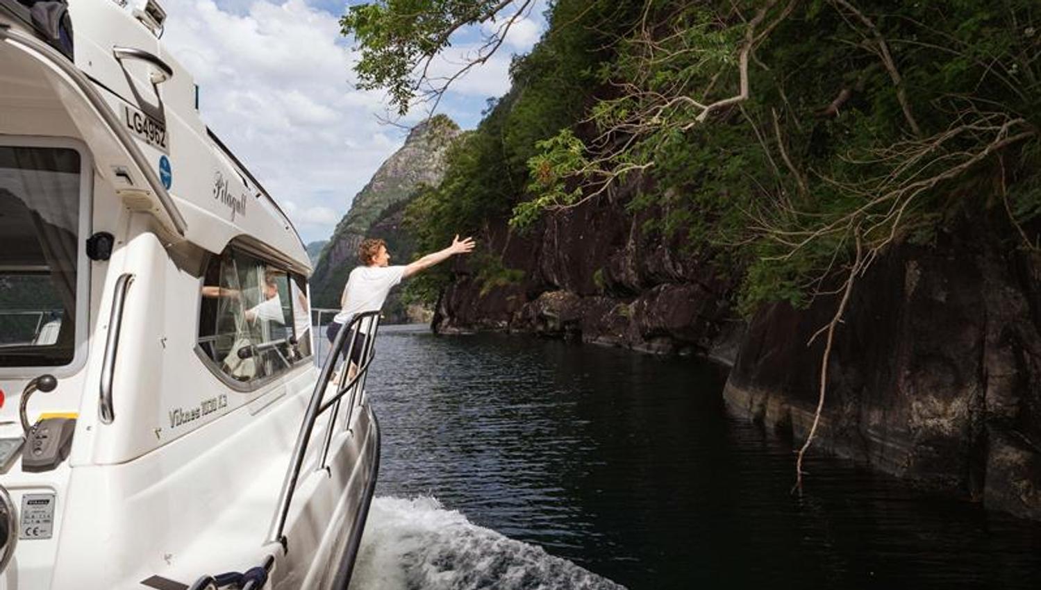 A guest enjoys the fjord cruise aboard Pilagutt as the boat navigates through narrow fjords with spectacular scenery.