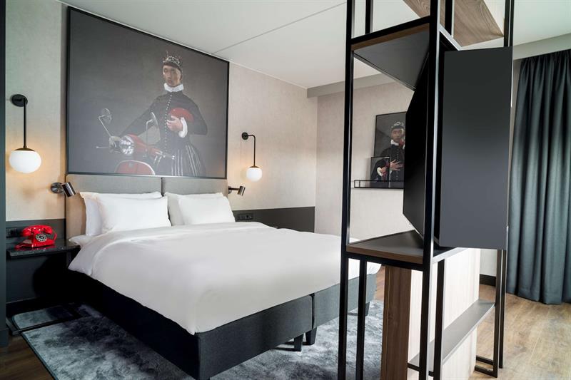 Superior room with a double bed, large painting on the wall, light-tight curtains and shelf in front of the bed