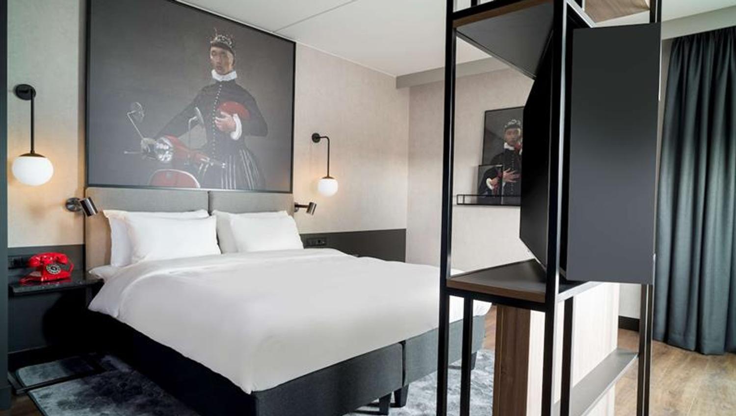 Superior room with a double bed, large painting on the wall, light-tight curtains and shelf in front of the bed
