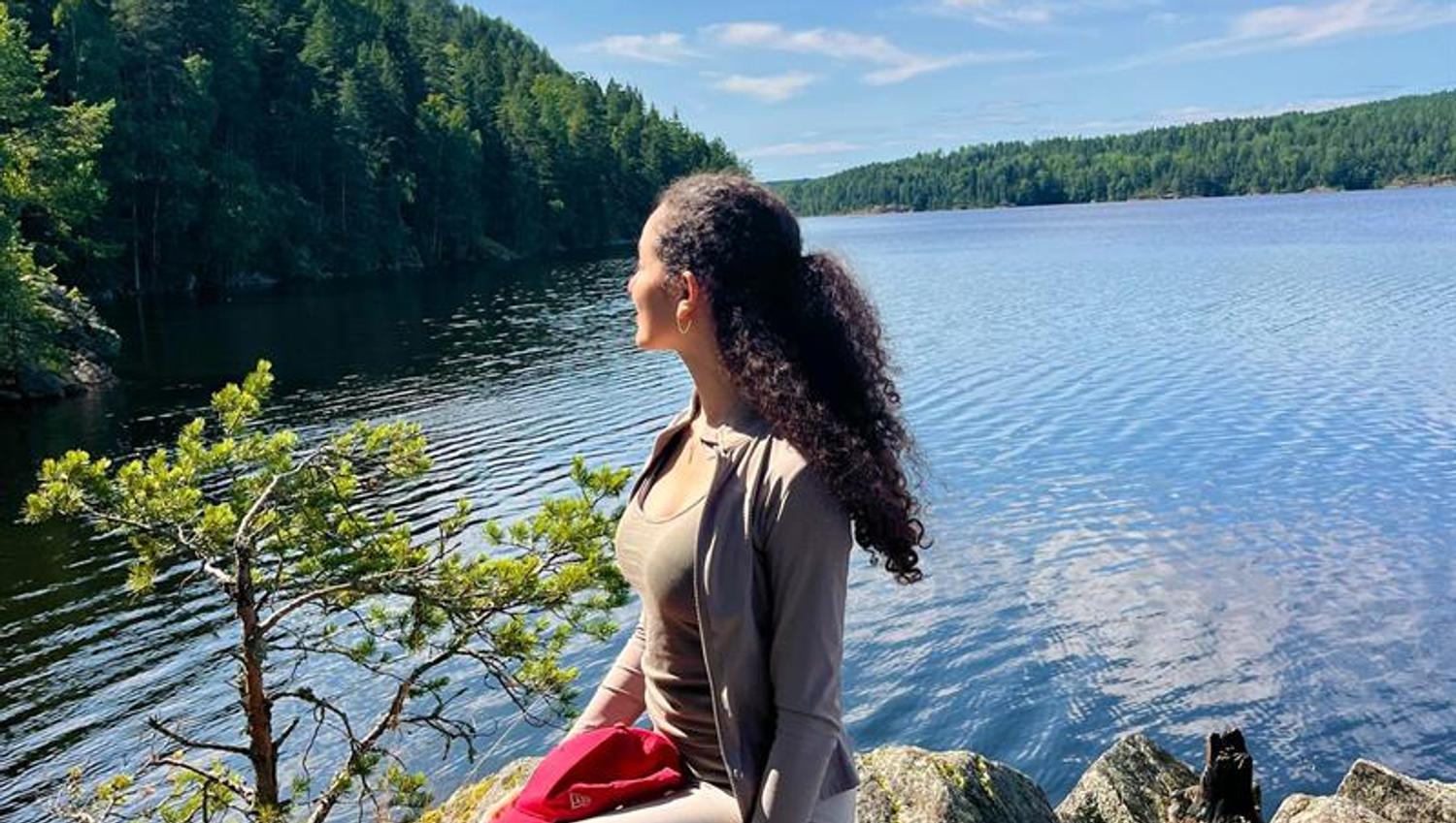 Girl sitting by a lake with the forest in the background
