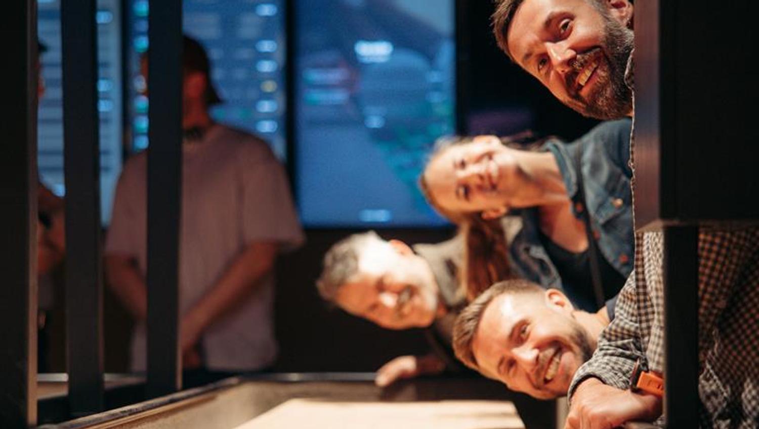 Smiling friends leaning over a shuffleboard table, watching the puck in a social gaming environment.
