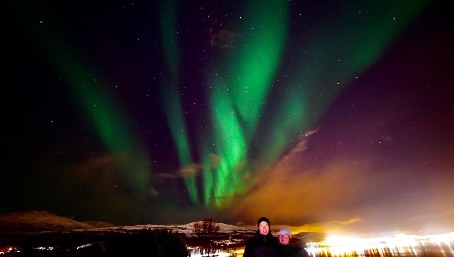 Two guests posing under the northern lights