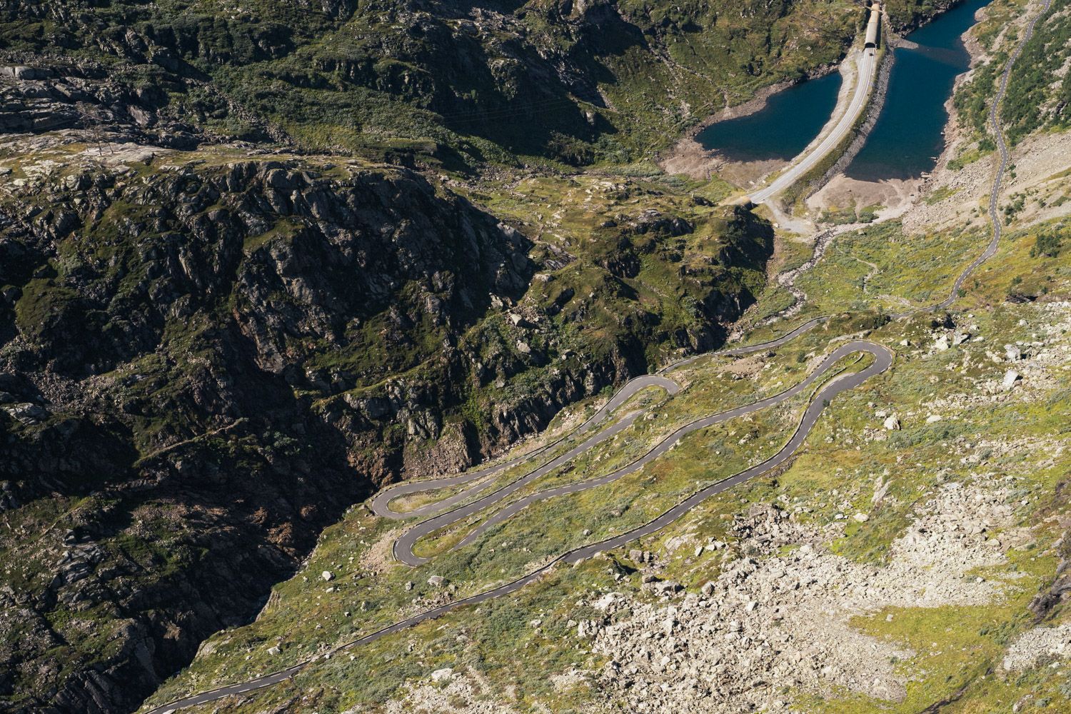 Fjellandskap med mykje grøntområder, steinur, vatn og bilveg.