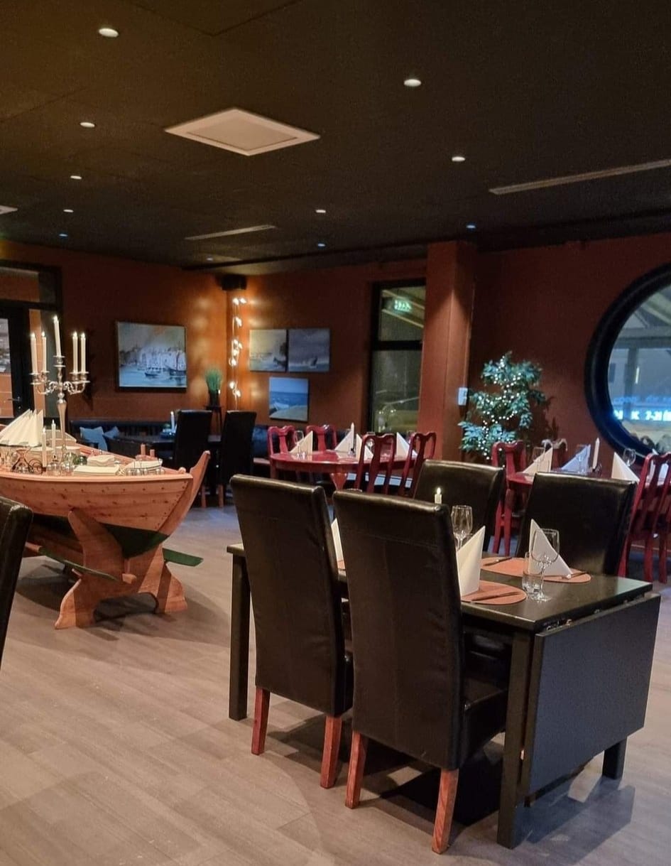 Interiørbilete av restauranten hos Gjøa Sjømat, med ein maritim stil og koselege oppdekka bord klare for gjestar.