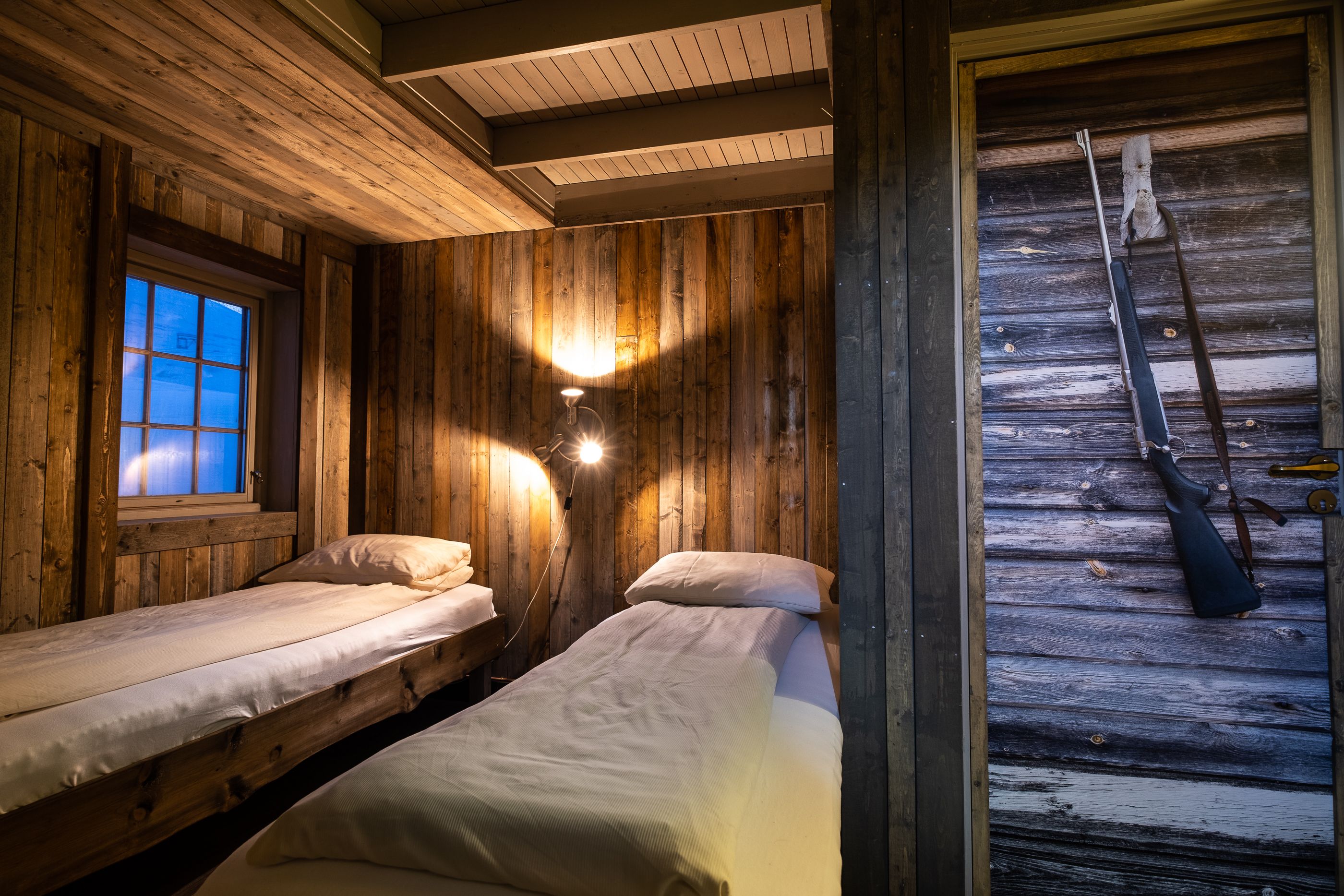 Interior photo of a bedroom at Tommy's Lodge, with two beds in the background and a photo of a rifle on a door in the foreground