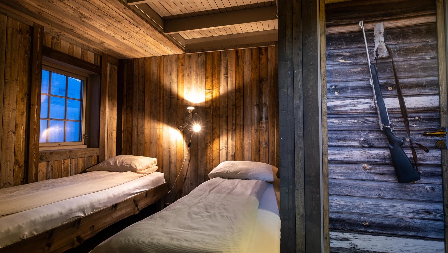 Interior photo of a bedroom at Tommy's Lodge, with two beds in the background and a photo of a rifle on a door in the foreground