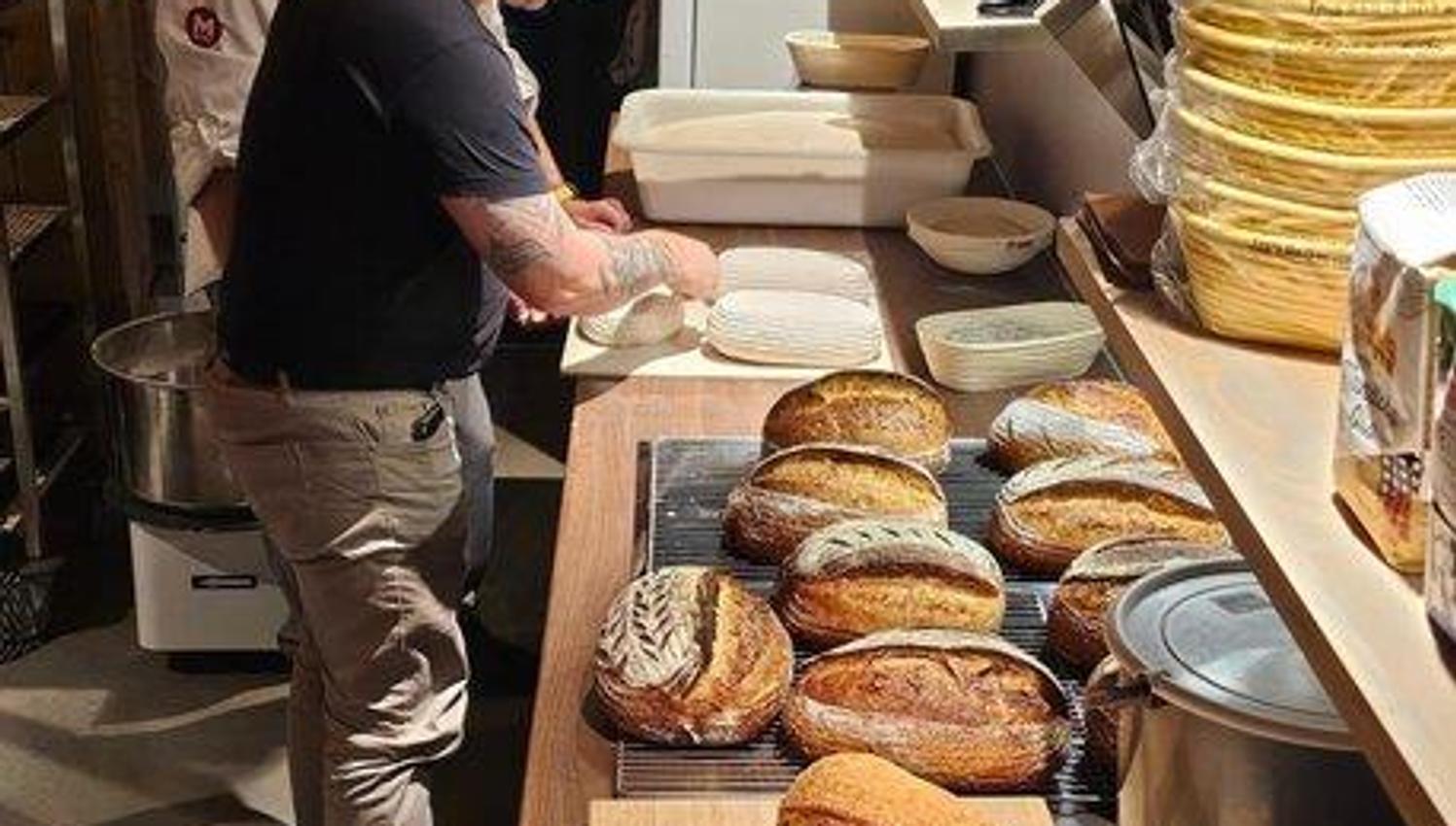 Two smiling men baking bread. Several freshly baked loaves on the counter in front of them.