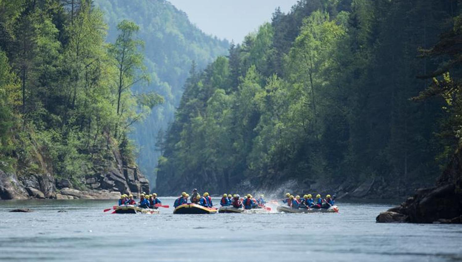 Vier Gruppen mit Raftingbooten, die im Wasser spielen.