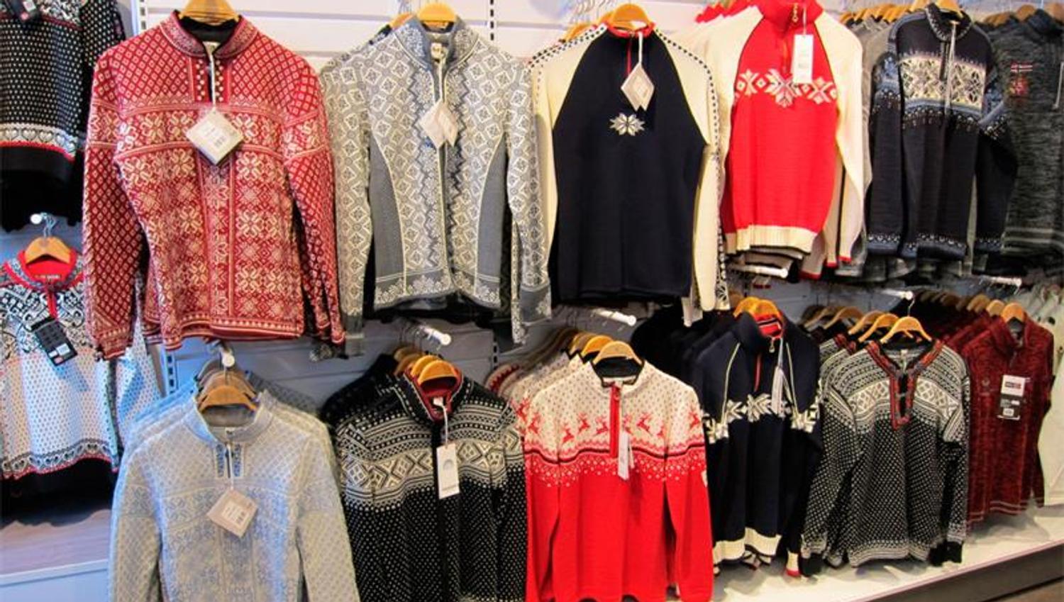 Diverse strikkede gensere som henger på stativ.