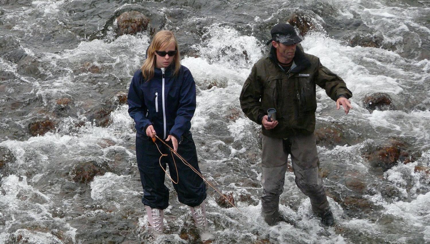 A man and a girl fishing in a river.