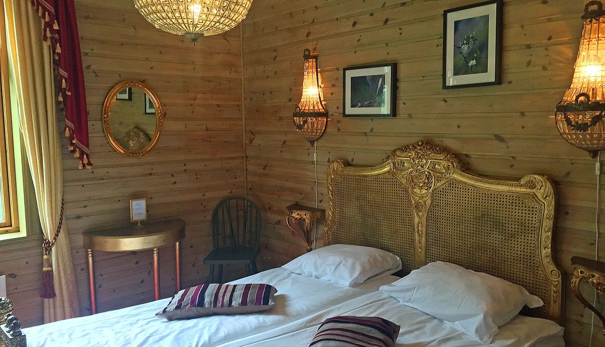 A room with a double bed, golden details and a big chandelair hanging above the bed.