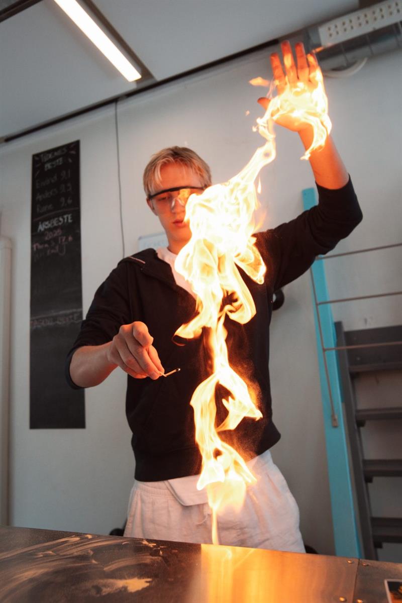 Elev med vernebriller held opp ei stor flamme under eit ildshow på KraftLaben vitensenter i Odda, Hardanger.