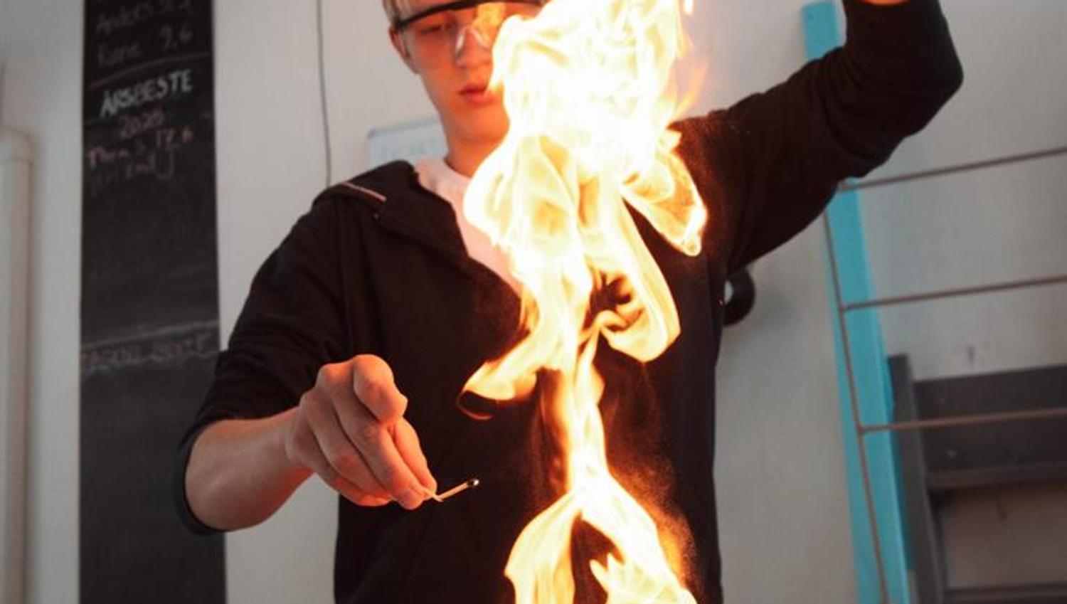 Elev med vernebriller held opp ei stor flamme under eit ildshow på KraftLaben vitensenter i Odda, Hardanger.